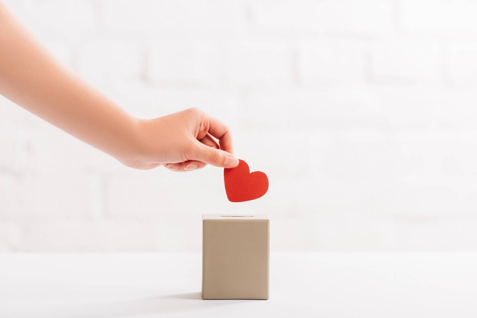 cropped view of female hand putting red heart in box on white background, donation concept